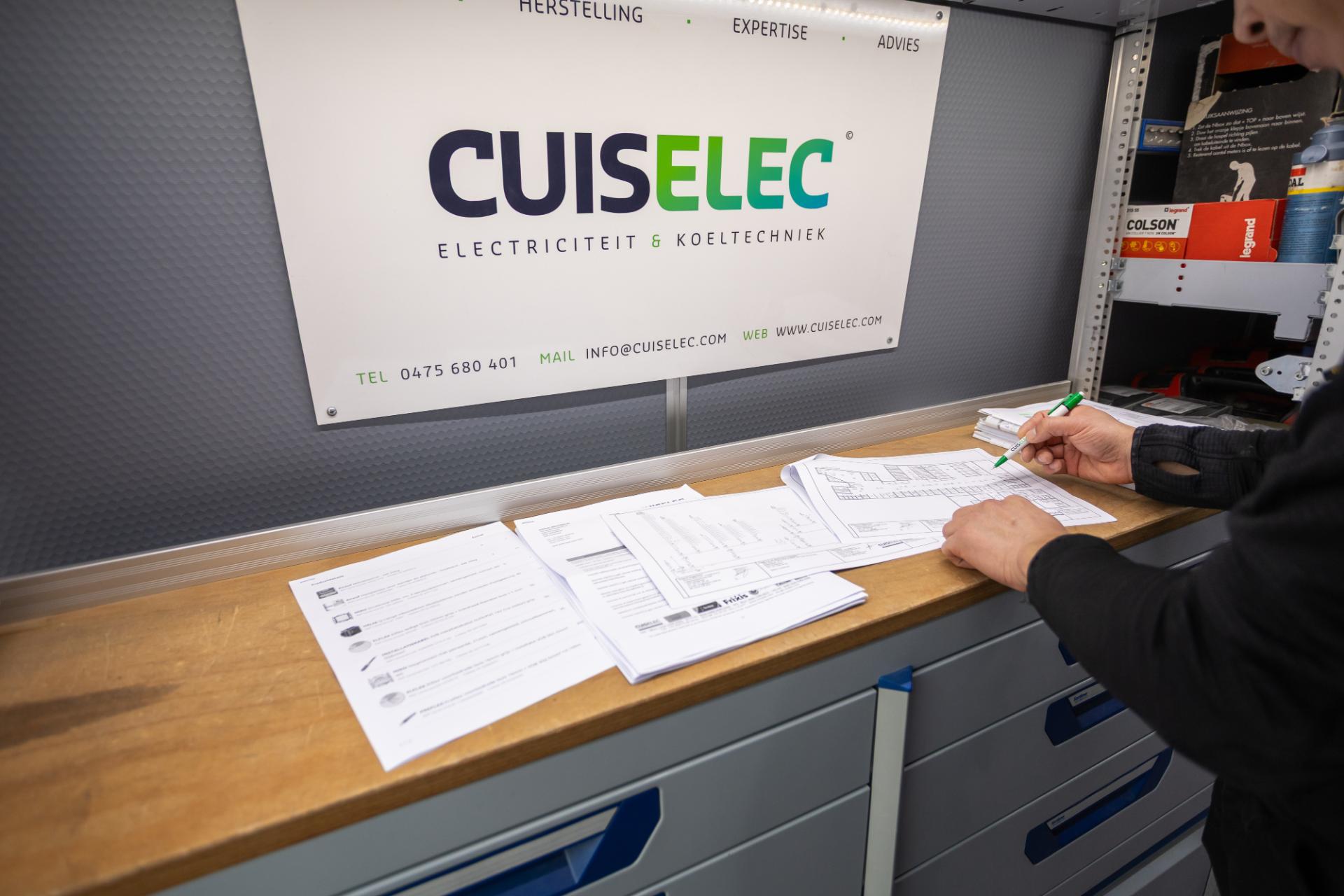 Elektricien bekijkt en noteert plannen op werkbank in servicewagen