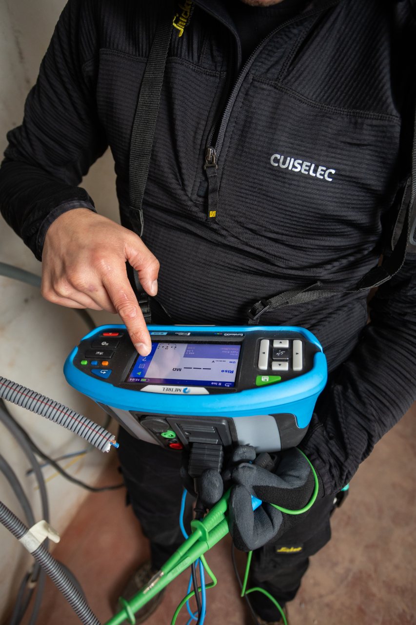 Technieker van Cuiselec controleert een elektrische installatie met een meettoestel vóór de herkeuring